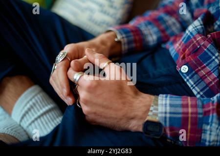 Primo piano di un uomo con le mani chiuse che indossa anelli d'argento, camicia a scacchi, calze bianche e jeans. Foto Stock