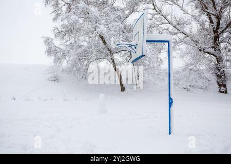 Anello di basket in strada in una fredda mattina d'inverno, fuori stagione. Un campo da basket coperto di neve. Concetto sportivo Foto Stock