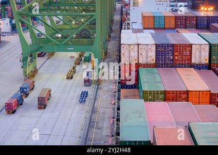 Vista sopraelevata di un affollato terminal container con container colorati impilati e camion merci operativi durante il crepuscolo, Singapore Foto Stock