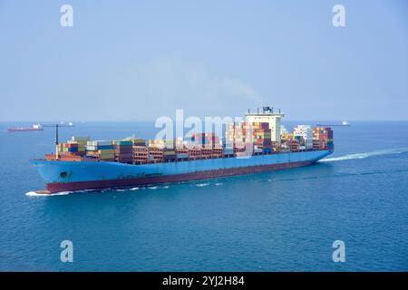Una grande nave cargo carica di contenitori colorati naviga attraverso l'oceano blu sotto un cielo limpido, il Mar Cinese meridionale Foto Stock