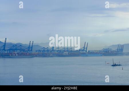 Vista nebbiosa di un porto con gru e una piccola barca sulle acque tranquille all'alba, Busan, Corea Foto Stock