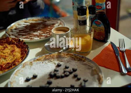 Una deliziosa colazione a buffet con crepe fresche con condimenti, una tazza di caffè e un bicchiere di succo d'arancia su un tavolo. Foto Stock