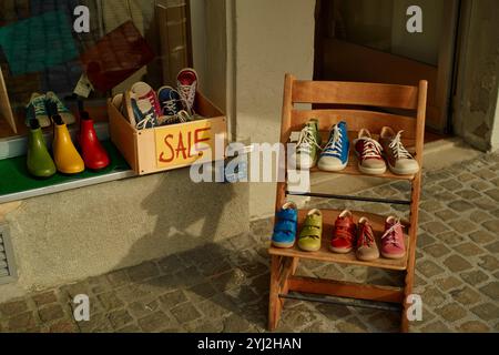 Scarpe colorate in vendita esposte all'esterno di un negozio in una giornata di sole, con paia disposte in modo ordinato su una sedia di legno e in una scatola. Foto Stock