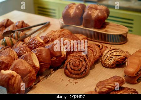 Una varietà di dolci appena sfornati esposti su un ripiano in legno, tra cui croissant, panini e dolcetti tortuosi. Foto Stock