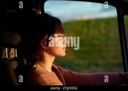 Una donna concentrata che guida un'auto durante un'ora d'oro, che getta una calda luce solare sul suo profilo. Foto Stock