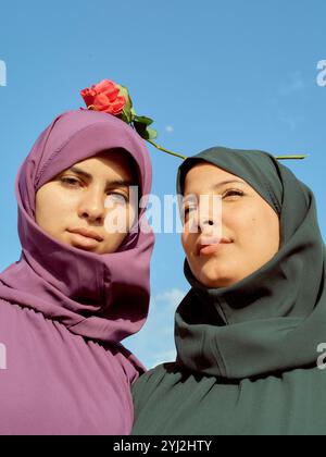 Due donne che indossano colorate hijab posano con una rosa contro un cielo blu limpido, il Marocco Foto Stock