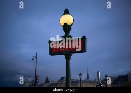 Insegna della metropolitana illuminata su un cielo scuro con la silhouette dello skyline della città sullo sfondo. Foto Stock