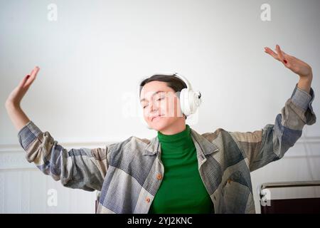 Donna che ascolta la musica con gli occhi chiusi e le cuffie accese mentre gesti con le mani in una stanza. Foto Stock
