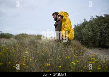 Un uomo e una donna in piedi in un campo con fiori selvatici gialli, la donna con un impermeabile giallo, Belgio Foto Stock