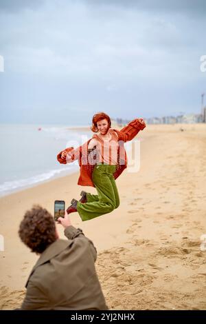 Una donna gioiosa salta su una spiaggia mentre un uomo scatta la sua foto con uno smartphone, Belgio Foto Stock