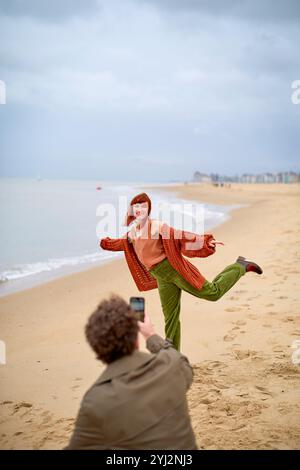 Persona che posa per una foto su una spiaggia di sabbia scattata da un fotografo accovacciato in primo piano, in Belgio Foto Stock