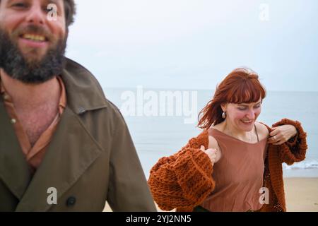 Uomo sorridente con barba e donna dai capelli rossi che si godono una passeggiata sulla spiaggia, in Belgio Foto Stock