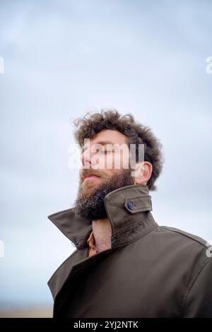 Primo piano di un uomo barbuto con gli occhi chiusi, respirando aria all'aperto, indossando una giacca marrone, Belgio Foto Stock