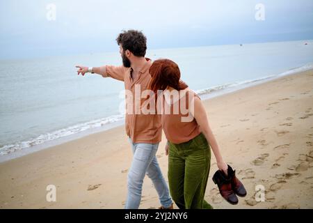 Un uomo e una donna che camminano a piedi nudi su una spiaggia sabbiosa, con l'uomo che punta verso il mare, in Belgio Foto Stock