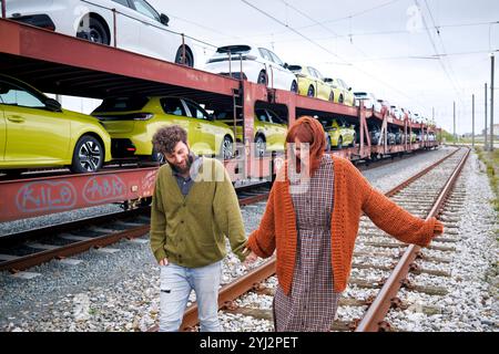 Un uomo e una donna camminano lungo i binari ferroviari accanto a un treno carico di auto colorate, il Belgio Foto Stock