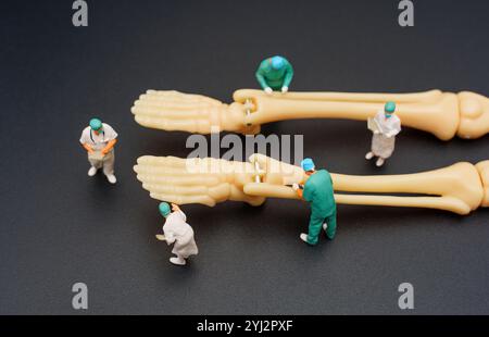 Scena creativa con figure di chirurgo in miniatura che lavorano su piedi di scheletro umano, ambientate su uno sfondo scuro, perfette per l'istruzione o l'illustrazione Foto Stock