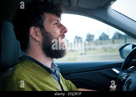 Uomo con la barba che guida un'auto in una giornata di pioggia, concentrandosi sulla strada davanti. Foto Stock