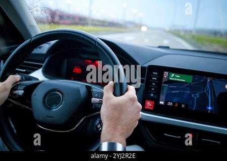 Primo piano delle mani del conducente sul volante con un cruscotto e uno schermo di navigazione in primo piano. Foto Stock