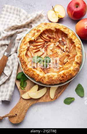 galette di mele appena sfornata decorata con scaglie di mandorle e menta, servita su un tavolo con mele fresche e un coltello Foto Stock