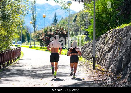 Una coppia che fa jogging su un sentiero panoramico circondato dal verde, abbracciando uno stile di vita attivo. Le montagne sullo sfondo aggiungono motivazione e bellezza Foto Stock