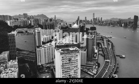 Un'ampia prospettiva aerea cattura Victoria Bay, evidenziando lo skyline di Hong Kong e l'attività marittima sotto i cieli nuvolosi. Foto Stock