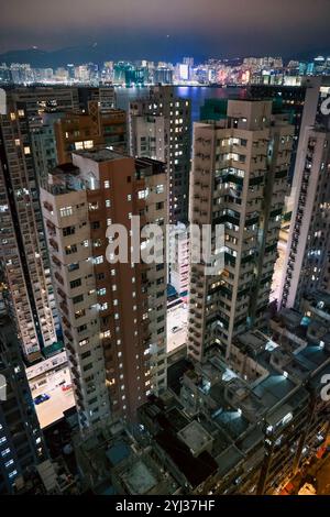 Lo skyline presenta alte strutture illuminate contro il cielo notturno, evidenziando la vivace vita urbana di Hong Kong. Foto Stock