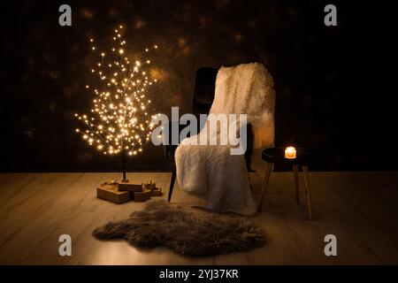 Concetto alternativo dell'albero di Natale. Struttura metallica minimalista di colore nero con luci illuminate di notte. Poltrona nera, plaid bianco, si presenta sotto il Foto Stock