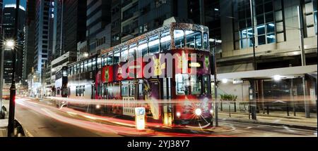 Un vivace tram viaggia attraverso le strade illuminate di Hong Kong, mostrando il suo design colorato sullo sfondo urbano vivace. Foto Stock
