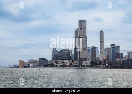 Un panorama mozzafiato rivela lo skyline di Hong Kong con grattacieli torreggianti sullo sfondo di cielo coperto e acque tranquille. Foto Stock