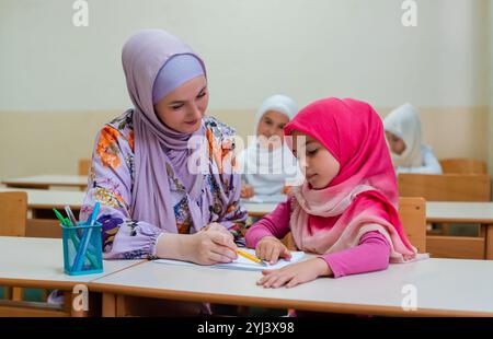 Insegnante musulmana hijab femminile aiuta il bambino a finire la lezione durante la lezione in classe. Foto Stock