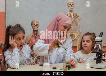 Bambini scienziati con un'insegnante musulmana che fa esperimenti scientifici di chimica nel laboratorio scolastico. Foto Stock