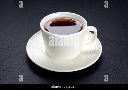 Una tazza di tè nero in una tazza di ceramica bianca su sfondo nero. Foto Stock