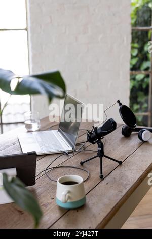 Configurazione dell'ufficio domestico con computer portatile, microfono e caffè su una scrivania in legno Foto Stock