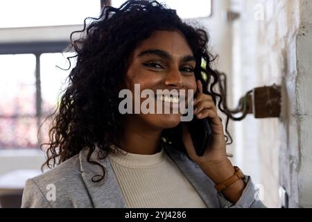 Donna sorridente che parla con lo smartphone a casa, godendo di una piacevole conversazione Foto Stock