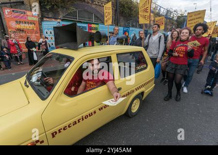 Londra, Regno Unito. 23 settembre 2017. Il Reliant Robin giallo brillante "Precarious Workers Mobile" di recente acquisizione, dotato di un potente amplificatore e altoparlante, guida gli scioperanti e i sostenitori di Ritzy in una lenta marcia intorno al centro di Brixton, mentre celebrano un anno di sciopero. Gli scioperanti del BECTU chiedono che il salario di sussistenza di Londra, la retribuzione per malattia, la retribuzione per maternità e paternità, che i dirigenti, i supervisori, gli chef e il personale tecnico siano adeguatamente valutati per il loro lavoro, e che i quattro rappresentanti sindacali licenziati siano reintegrati. Foto Stock