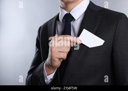 Uomo che prende un biglietto da visita vuoto dalla tasca della giacca su sfondo grigio, primo piano. Mockup per il design Foto Stock