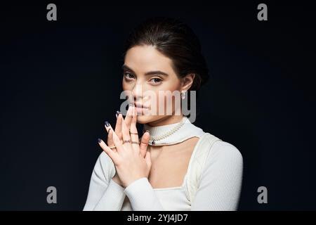 Una giovane donna posa elegantemente con un'espressione contemplativa, mani accuratamente posizionate. Foto Stock