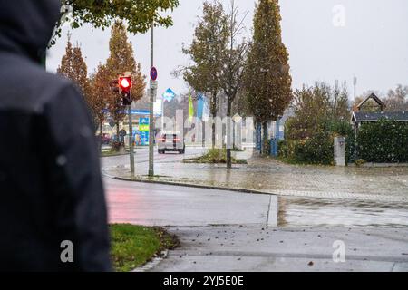 Langweid, Baviera, Germania - 13 novembre 2024: Immagine simbolica dei cambiamenti climatici e delle nevicate in Baviera. Un uomo con un cappuccio e una giacca invernale cammina vicino a una strada con il tempo nuvoloso *** Symbolbild Wetterumschwung und Schneefall a Bayern. Ein Mann mit Kaputze und Winterjacke läuft bei trübem Wetter neben einer Straße spazieren Foto Stock