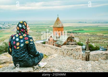 La giovane donna sul punto panoramico indossa un abbigliamento modesto siediti e goditi il viaggio visitando il famoso edificio del monastero e la cappella di Khor Virap. Viaggi e religiosi d Foto Stock