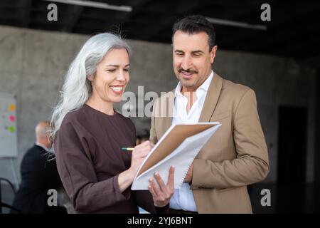 Una donna e un uomo si impegnano in una discussione collaborativa in un ufficio moderno. La donna scrive su un blocco note mentre l'uomo ascolta attentamente, entrambi smili Foto Stock