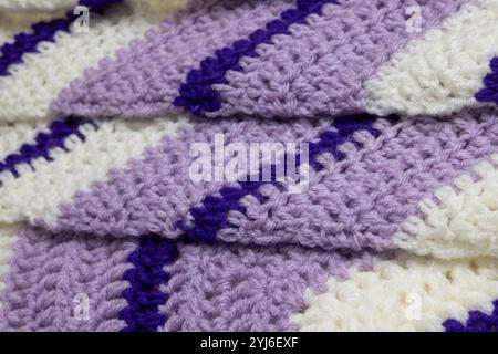 primo piano di coperte a zigzag viola lilla, bianco e viola reale con accenti bianchi e verdi cacciatori, all'uncinetto o a maglia, ricorda tutti Foto Stock