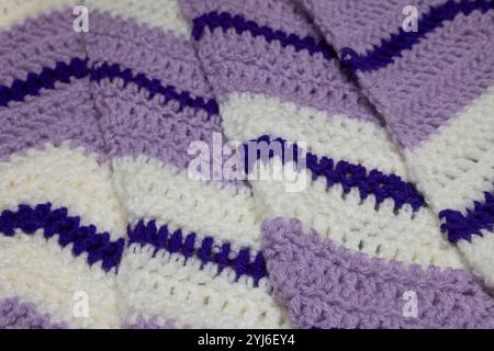 primo piano di coperte a zigzag viola lilla, bianco e viola reale con accenti bianchi e verdi cacciatori, all'uncinetto o a maglia, ricorda tutti Foto Stock