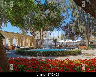 Bellissimo giardino con una fontana, archi e fiori rossi ai giardini Upper Barrakka di la Valletta, Malta. Foto Stock