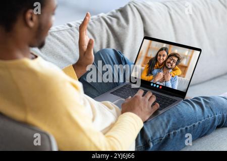 Due amici condividono un momento sentito durante una videochiamata su un laptop, mentre sono seduti su un comodo divano, trasmettendo calore e connessione in un ambiente intimo e rilassato Foto Stock