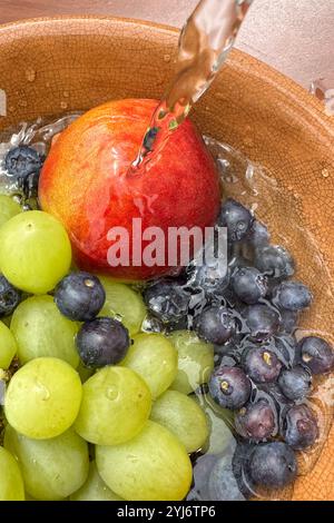 primo piano di frutta fresca, mirtilli, pesca e uva, in un recipiente sotto l'acqua corrente mentre si lava la frutta. Foto Stock