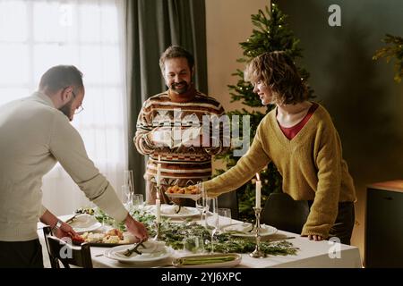 La famiglia caucasica serve tavoli decorati, mette piatti deliziosi su piatti bianchi e antipasti durante la preparazione per la festa di Natale Foto Stock