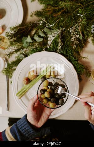 Colpo dall'alto di uomo irriconoscibile seduto al tavolo festivo e prendendo olive dalla ciotola di cristallo Foto Stock