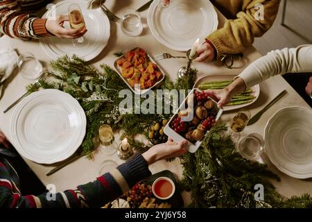 Foto dall'alto di amici irriconoscibili al tavolo decorato, bevendo spumante e mangiando cibo tradizionale per Natale Foto Stock