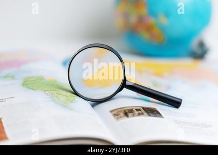 Lente d'ingrandimento su atlas con il globo sullo sfondo, che simboleggia gli studi geografici, l'apprendimento scolastico, l'esplorazione globale e l'acquisizione di conoscenze su WO Foto Stock