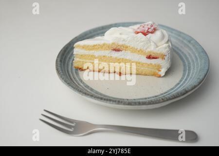 Una piccola shortcake giapponese alle fragole e una piccola forchetta su un elegante piatto giapponese su un tavolo bianco. Foto Stock